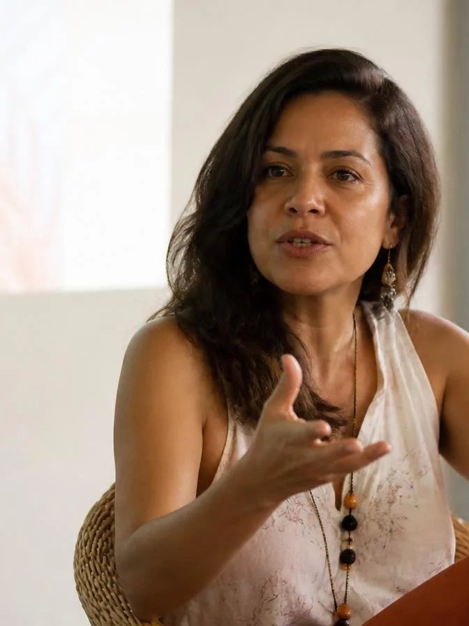 Participante com o braço levantado pedindo a vez numa mesa coberta de rascunhos